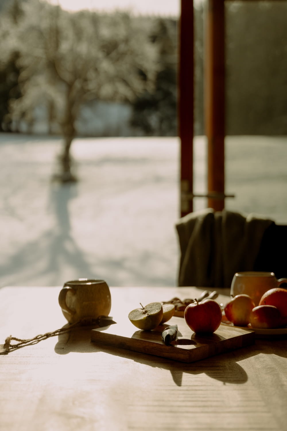 Äpfel und Tassen auf Holztisch mit Blick in die verschneite Landschaft im Allgäu.