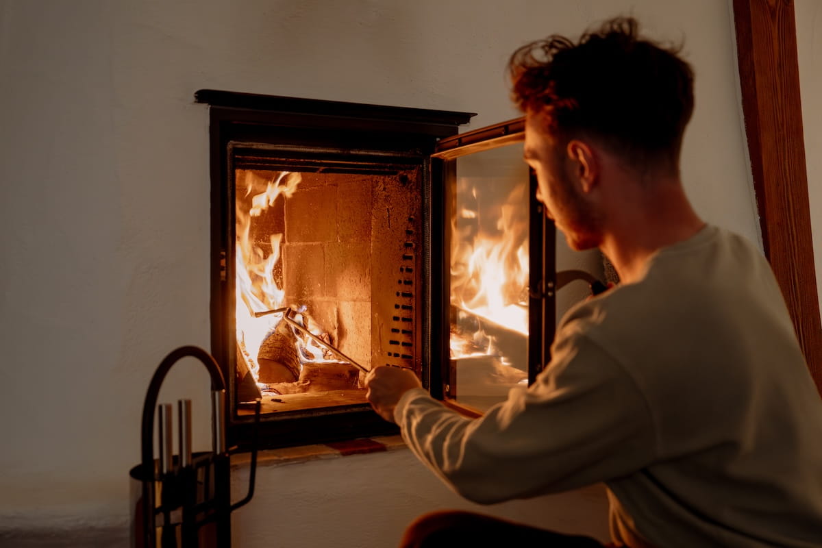 Ein Mann schürt mit einem Schürhaken das Feuer im geöffneten Kamin.